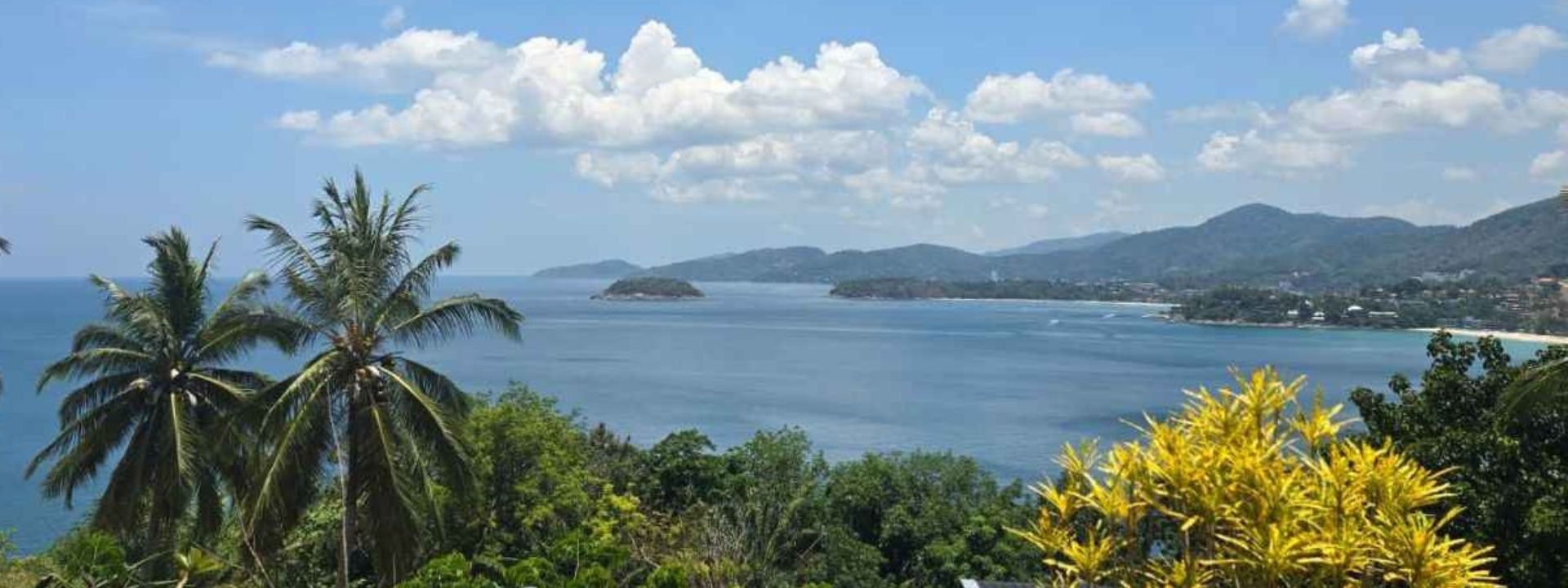 Coastal view of Phuket with palm trees, a small island and surrounding hills