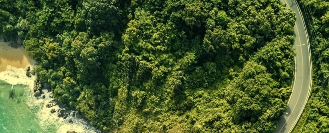 Aerial view of Phuket coastline with winding road and lush land area, illustrating land boundaries and terrain for property buyers.
