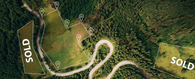 Aerial view of land plots outlined with markers and sold labels in a forested area.