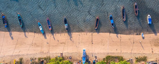 Aerial view of longtail boats lined up along the shoreline at Rawai Beach in Phuket