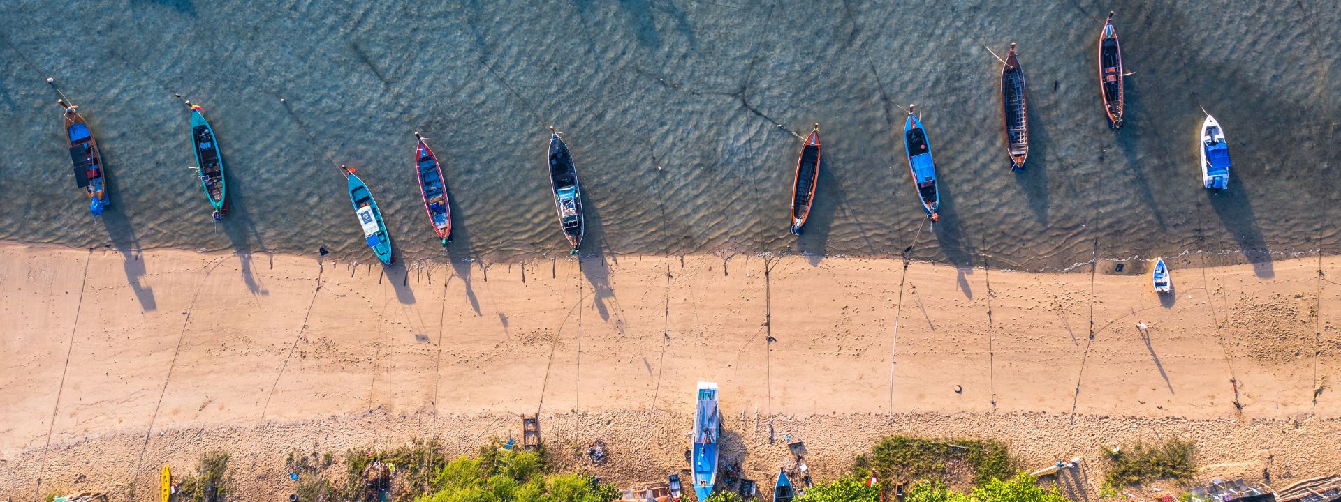 Aerial view of longtail boats lined up along the shoreline at Rawai Beach in Phuket