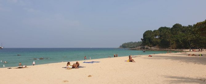 Surin Beach in Phuket with people relaxing on the sand and swimming in the water.