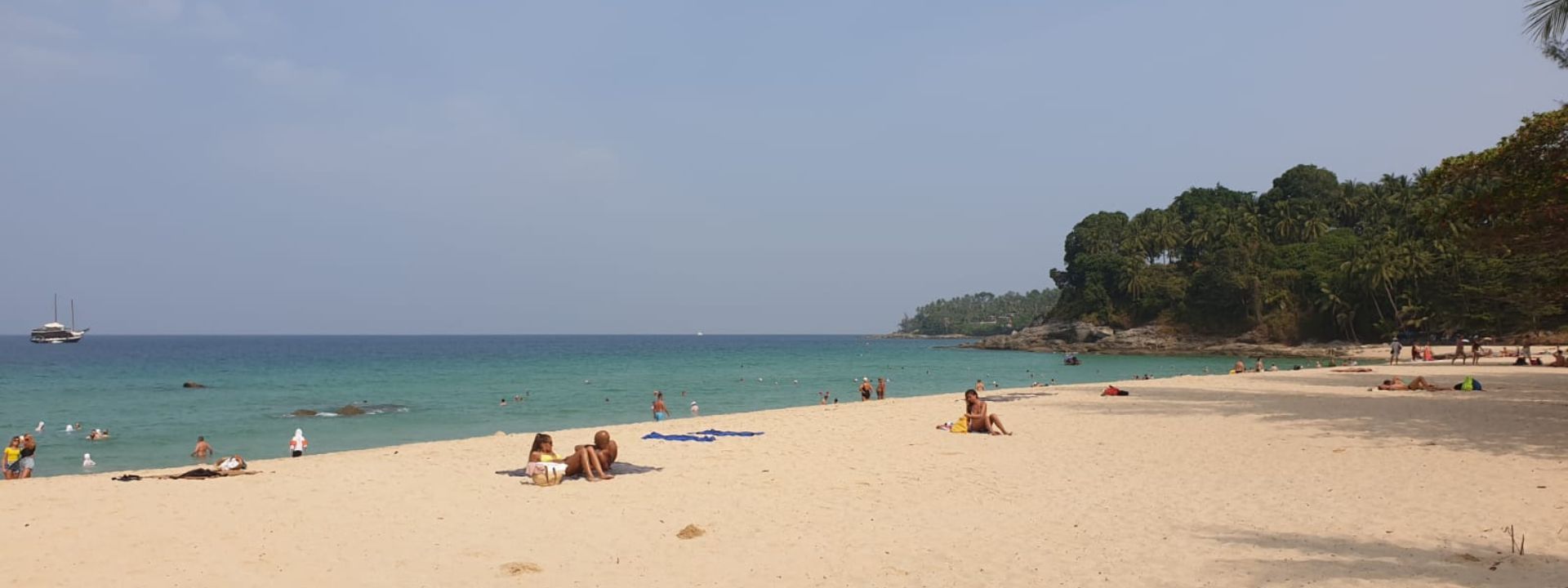 Surin Beach in Phuket with people relaxing on the sand and swimming in the water.