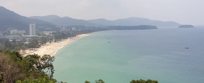 Aerial view of Karon Beach in Phuket with mountains, coastline and turquoise water.
