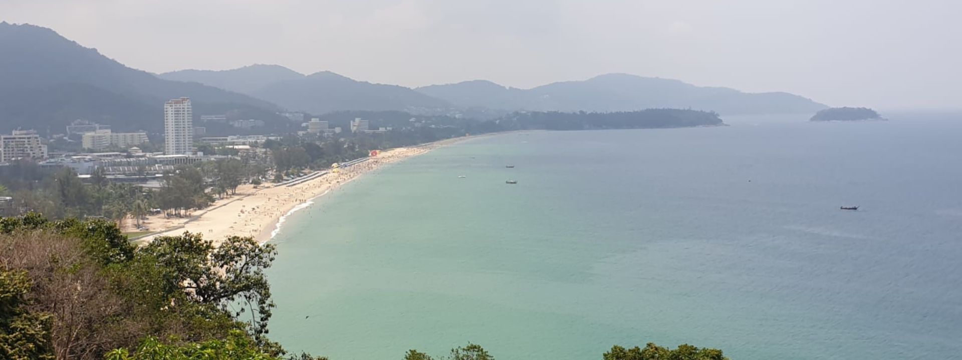 Aerial view of Karon Beach in Phuket with mountains, coastline and turquoise water.