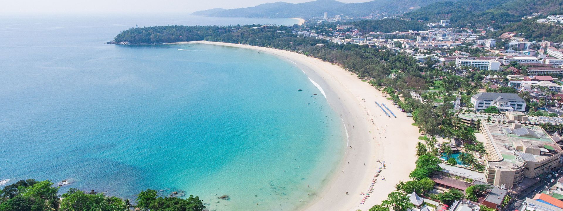 Aerial view of Kata Beach in Phuket with turquoise water, coastline and surrounding town.