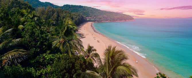 Tropical view of Nai Thon Beach in Phuket with turquoise water, soft sand and lush palm trees at sunset.
