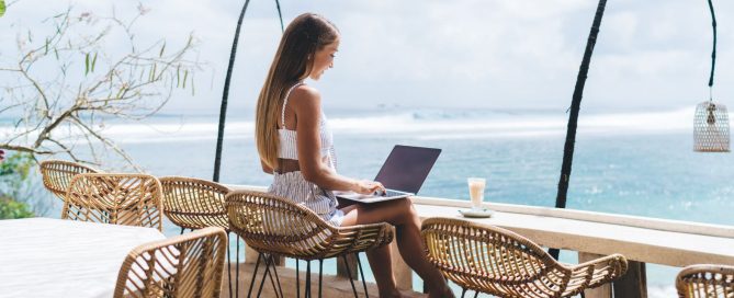 Digital nomad working on a laptop at a beachfront café in Phuket overlooking the ocean.