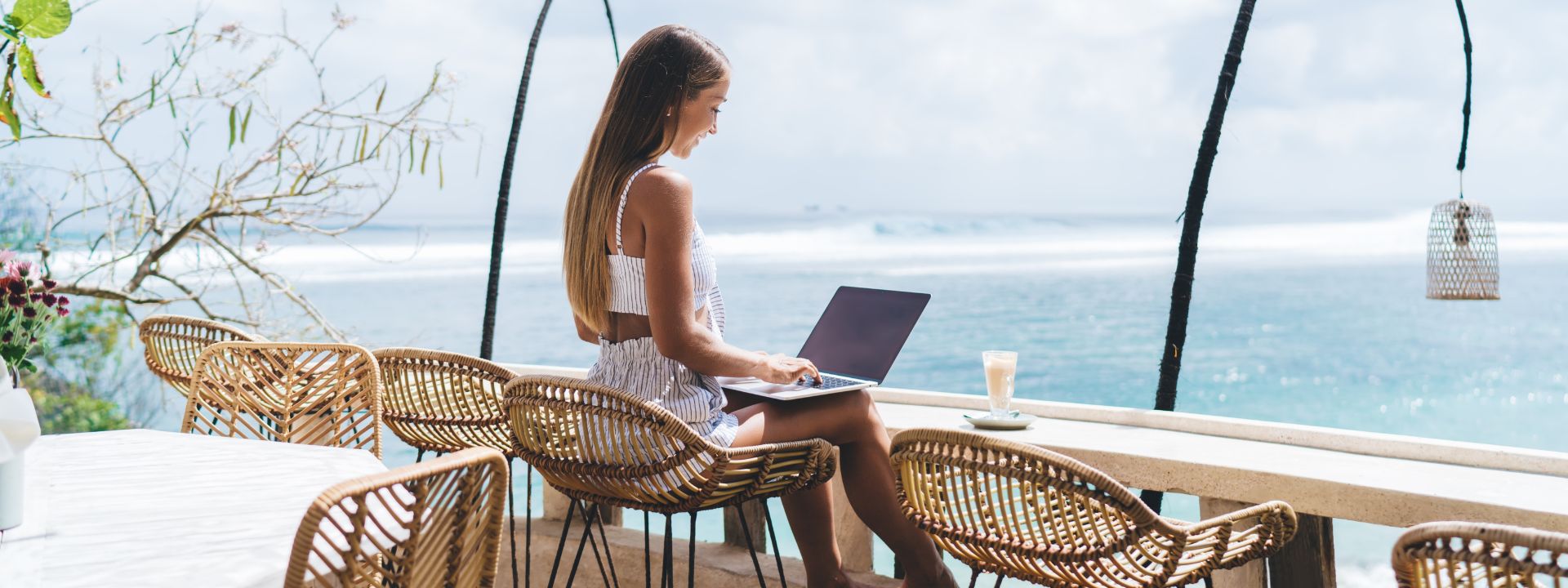 Digital nomad working on a laptop at a beachfront café in Phuket overlooking the ocean.