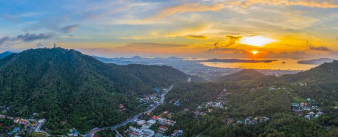 Panoramic aerial view of Phuket at sunrise with hills, coastline, and Chalong Bay