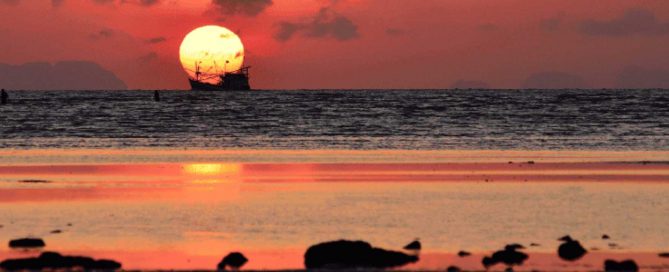 Sunset over the sea in Phuket with a silhouetted boat on the horizon