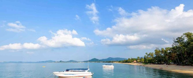 Calm coastal bay at Cape Panwa in Phuket with anchored boats and palm-lined shoreline