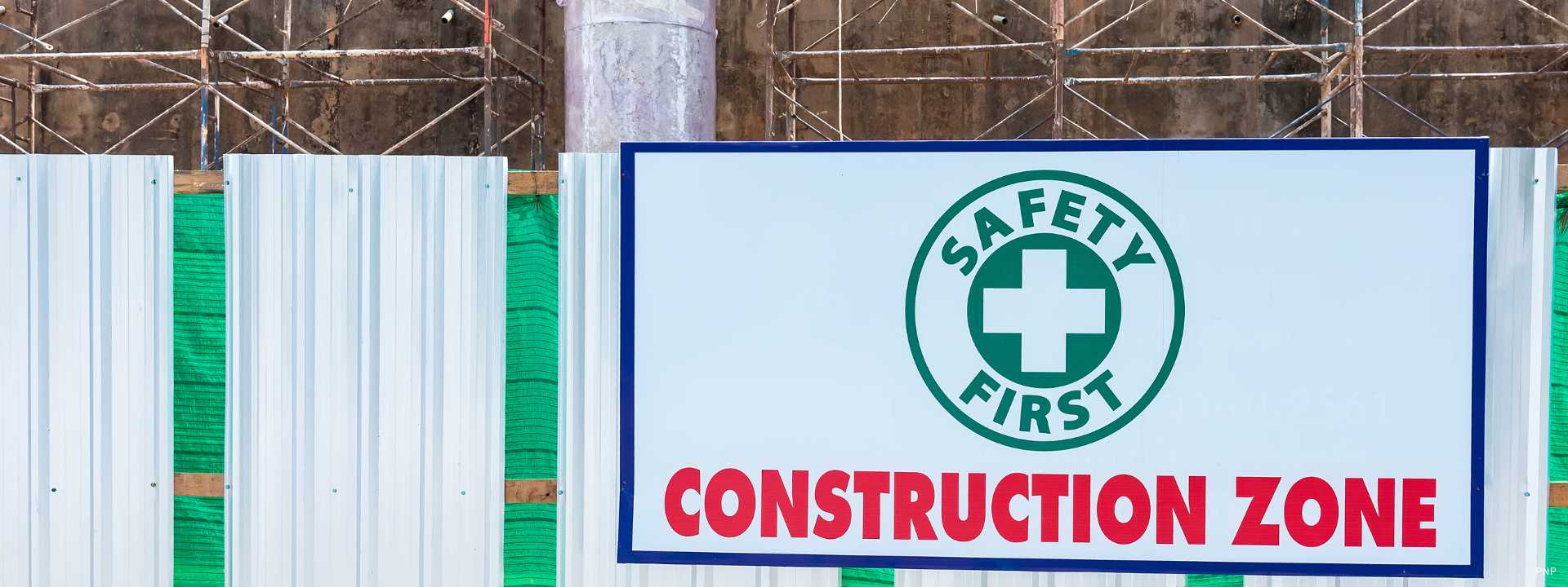 Alt text Construction zone safety sign displayed on a fenced building site with scaffolding in the background