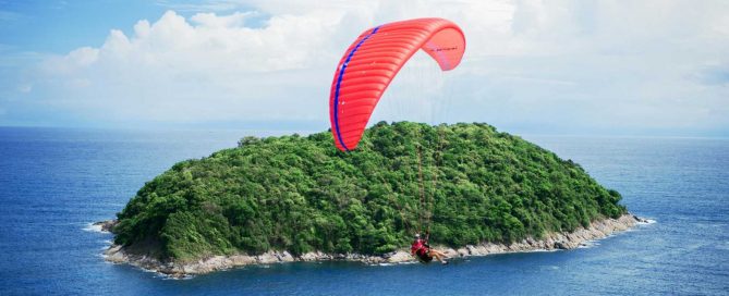 Paraglider flying above a small tropical island off the coast of Phuket, highlighting adventure tourism and island lifestyle appeal
