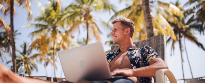 Digital nomad working remotely from Phuket with laptop under palm trees