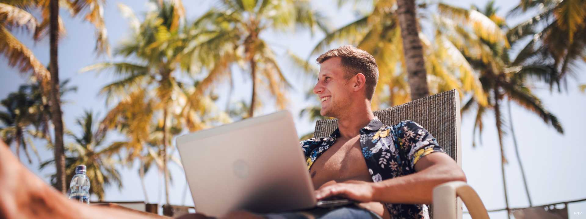Digital nomad working remotely from Phuket with laptop under palm trees