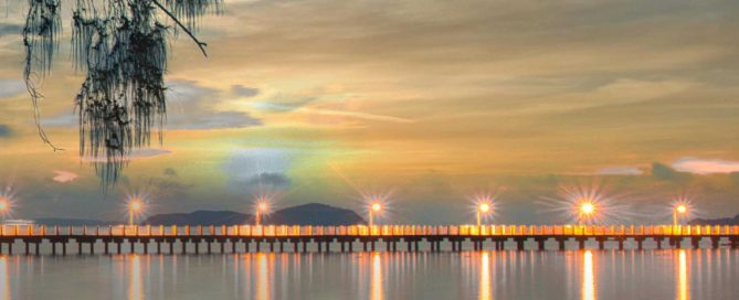 Pier in Phuket at dusk with illuminated lights reflecting across calm water