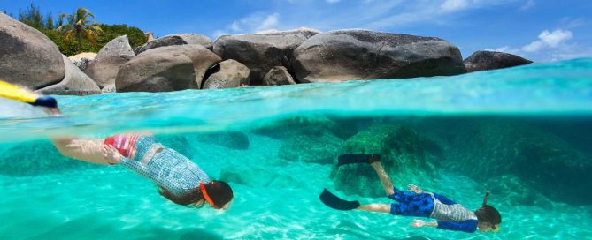 Snorkellers swimming in clear turquoise waters near rocky coastline in Phuket