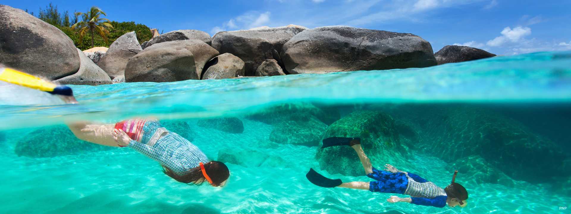 Snorkellers swimming in clear turquoise waters near rocky coastline in Phuket