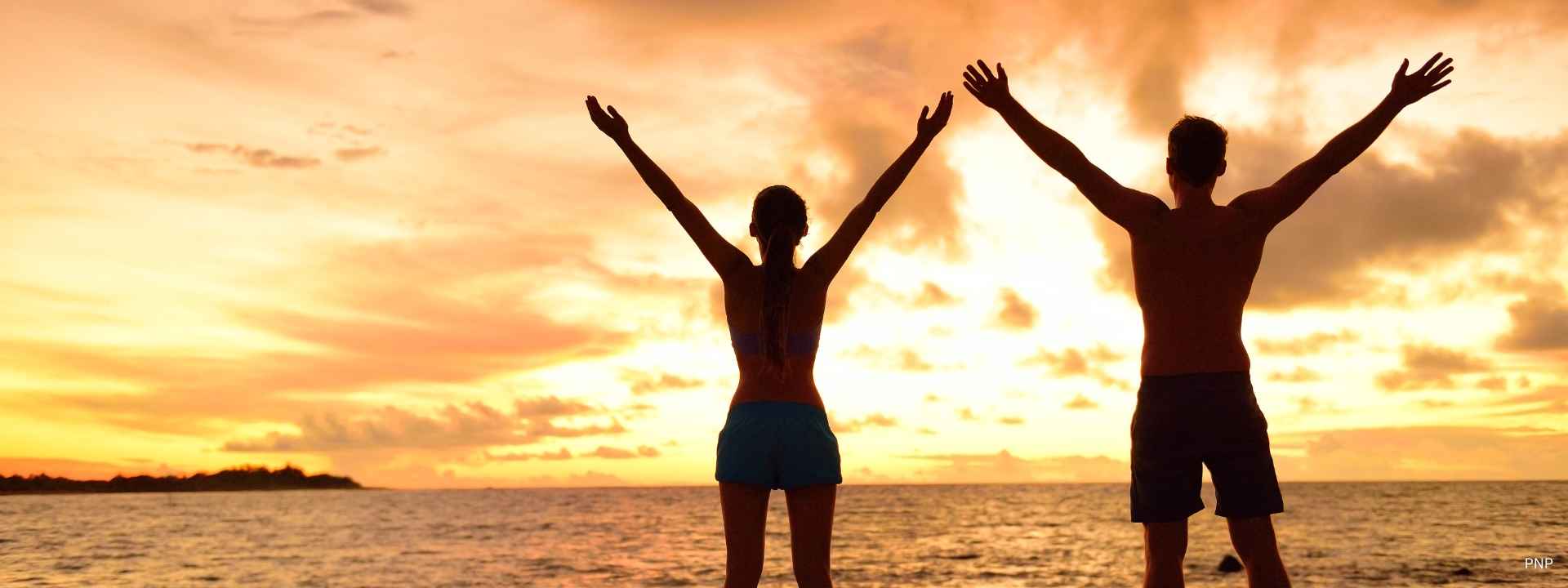 Couple standing on a Phuket beach at sunset with arms raised, enjoying coastal lifestyle