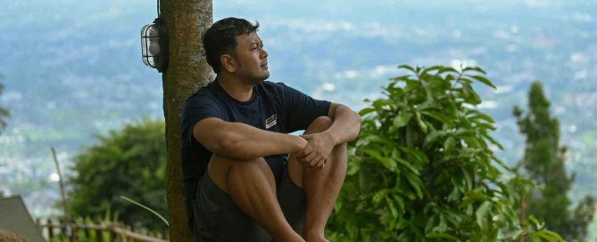 Man sitting outdoors overlooking Phuket hillside and town, reflecting in a natural setting