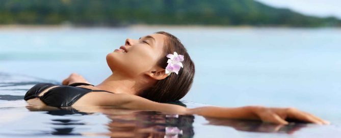 Woman relaxing in a swimming pool overlooking calm water and distant hills