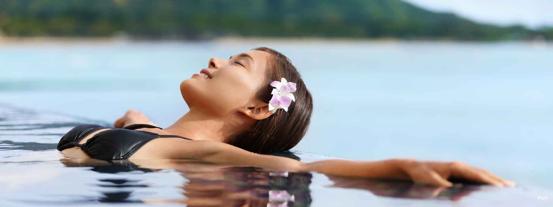 Woman relaxing in a swimming pool overlooking calm water and distant hills
