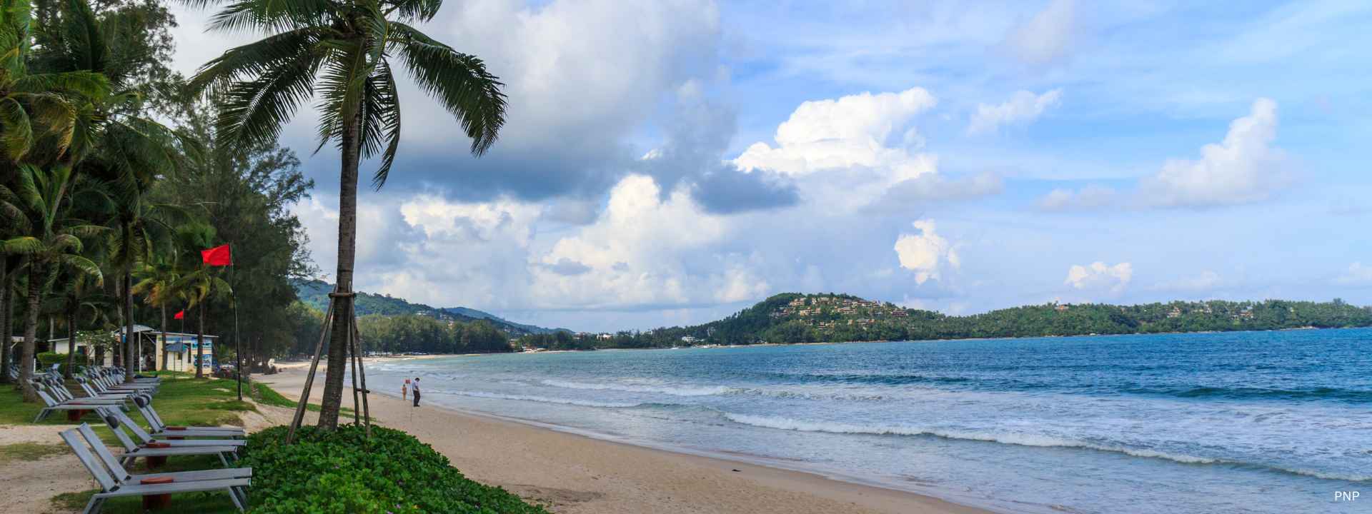 Peaceful beachfront in Bang Tao, Phuket with palm trees, sandy shoreline, and calm sea along a residential coastal area