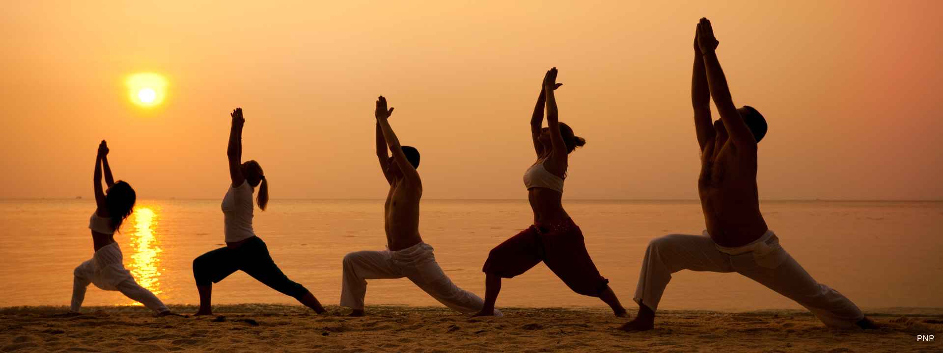 Group of people practising yoga on a beach at sunset by the sea