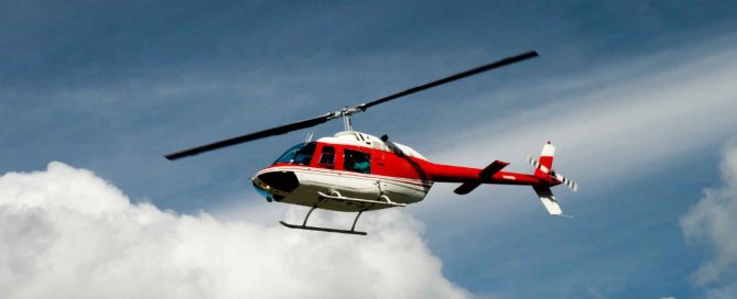Red and white helicopter flying in a blue sky with clouds