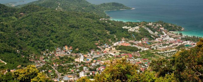 Panoramic aerial view of Karon Beach in Phuket with turquoise bay, hillside greenery, and coastal town below