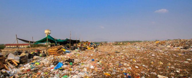 Large landfill site with piles of mixed waste, plastic debris, and temporary shelters under a clear sky