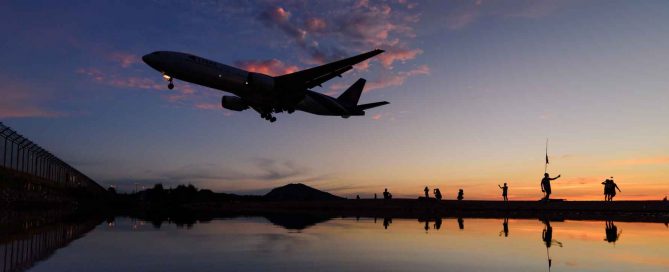 Airplane landing over Mai Khao Beach in Phuket at sunset with silhouettes of people watching and colourful evening sky