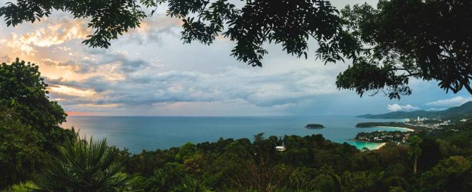 Elevated view of the Phuket coastline with the sea, green hills, tropical forest, and bays visible in the distance