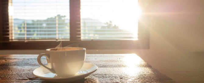 Sunlight streaming through a window onto a coffee cup on a wooden table, symbolising a calm morning in Phuket
