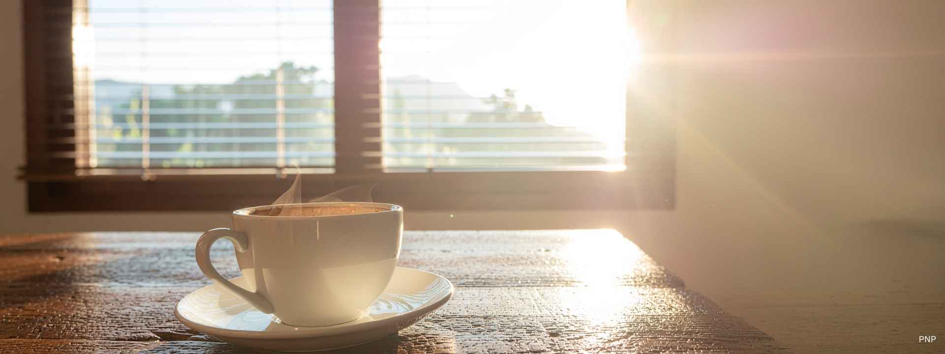 Sunlight streaming through a window onto a coffee cup on a wooden table, symbolising a calm morning in Phuket