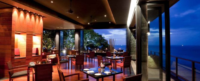 Elegant open-air restaurant in Phuket with wooden furnishings, ambient lighting, and ocean views at dusk