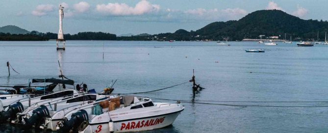 Parasailing speedboats moored in Patong Bay with calm sea, distant hills, and boats anchored offshore in Phuket