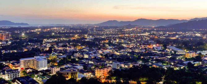 Panoramic view of Phuket Town at dusk with city lights, surrounding hills, and distant coastline