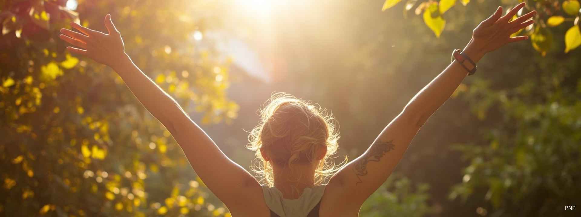 Woman standing in a sunlit forest with arms raised, enjoying the morning light in Phuket