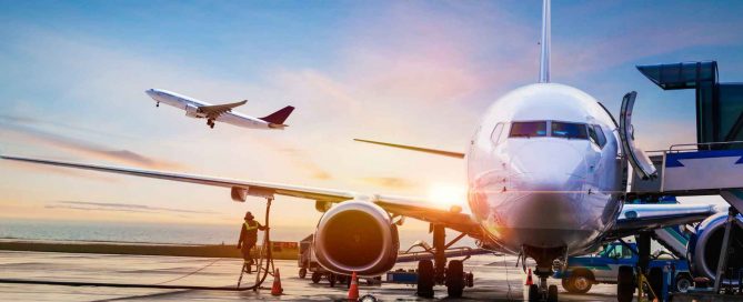 Commercial airplane being refueled on an airport runway at sunrise with another plane taking off in the background