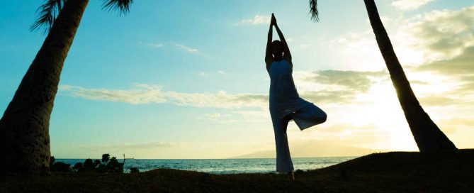 Person practicing yoga at sunrise on a tropical Phuket beach, reflecting a healthy and balanced lifestyle