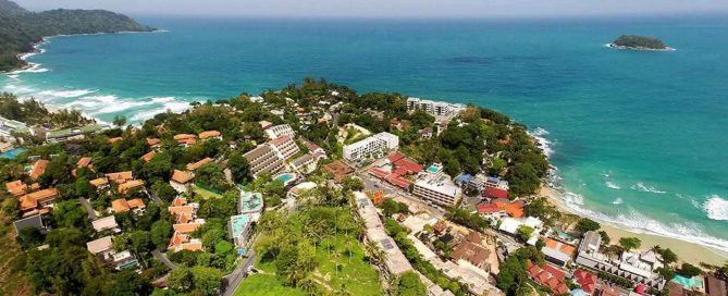 Phuket coastal headland developed with hillside villas and resorts, surrounded by sandy beaches, tropical greenery and an offshore island.